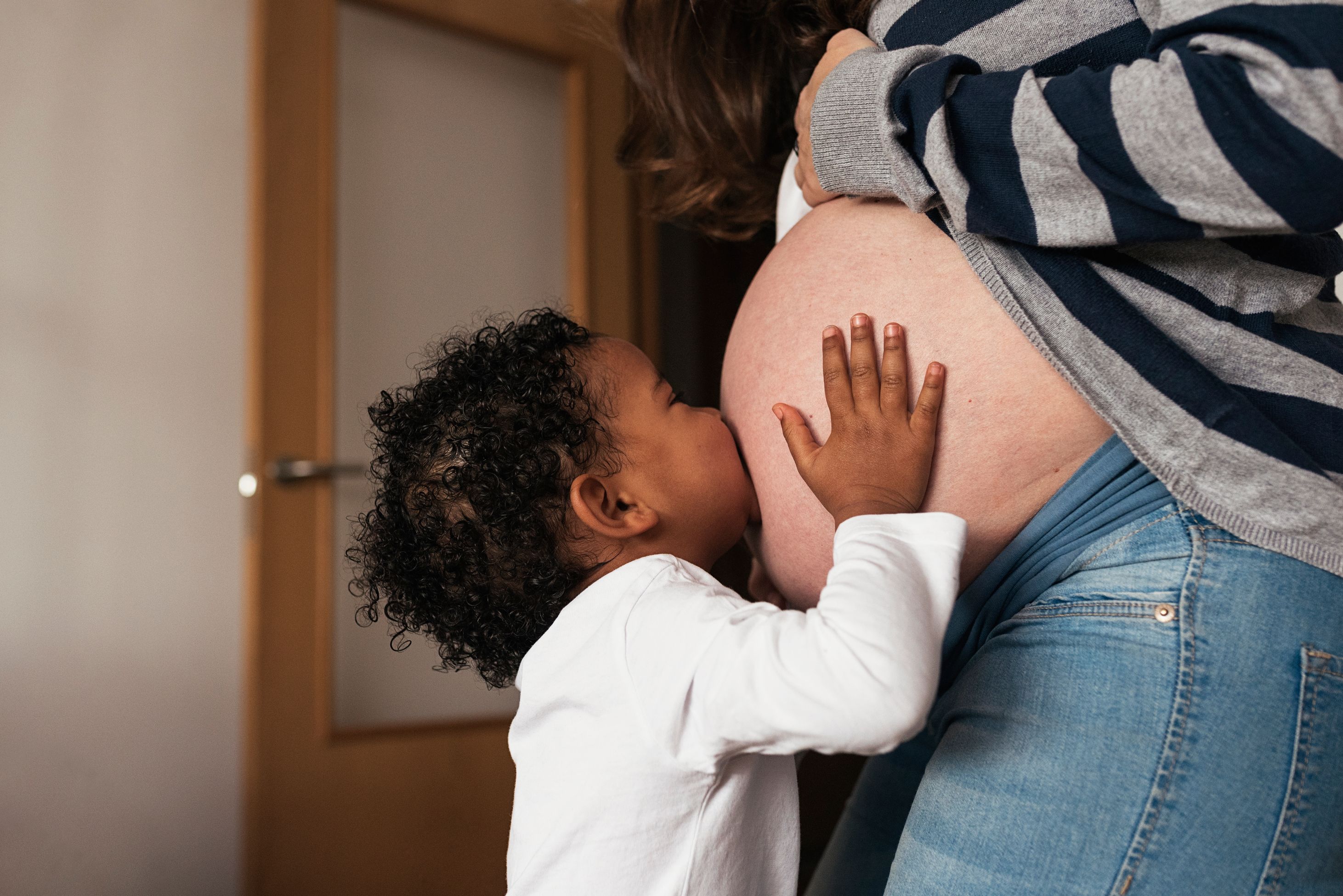 child holding and kissing mother's pregnant stomach